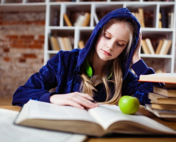 Uma aluna estudando na biblioteca com vários materiais escolares a sua volta