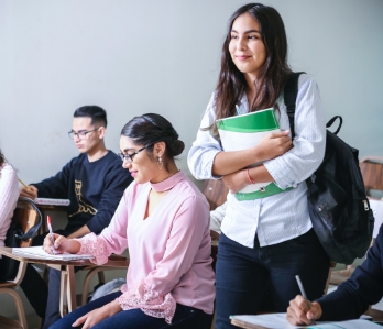 Estudante carregando sua mochila e material escolar, em pé, na sala de aula